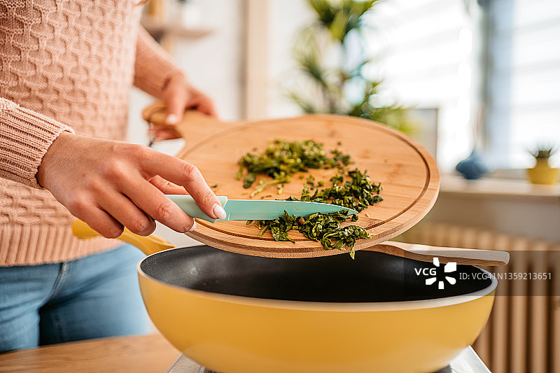 女人往煎锅里加菠菜图片素材