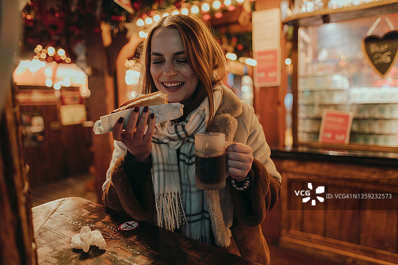 在圣诞市场吃香肠喝热红酒的女人图片素材