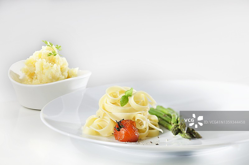 炒圣女果、罗勒、绿芦笋意大利宽面，背景是欧芹土豆泥图片素材