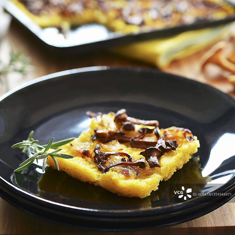 烤盘前盘子里放着一块搭配着鸡油菌和洋葱的玉米粥蛋糕图片素材