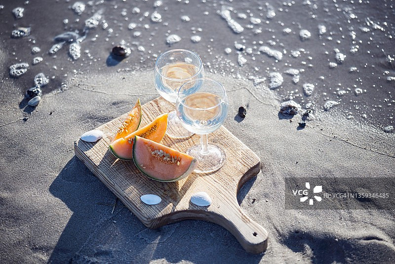 两杯白葡萄酒和哈密瓜在沙滩上图片素材
