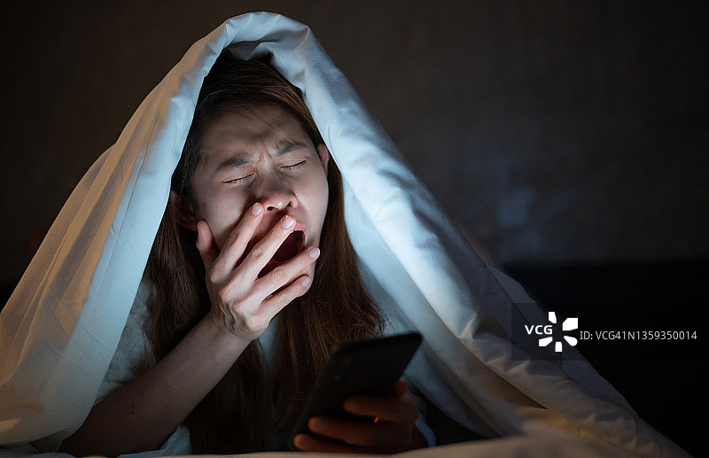 深夜在床上玩手机上网时打哈欠的女人图片素材