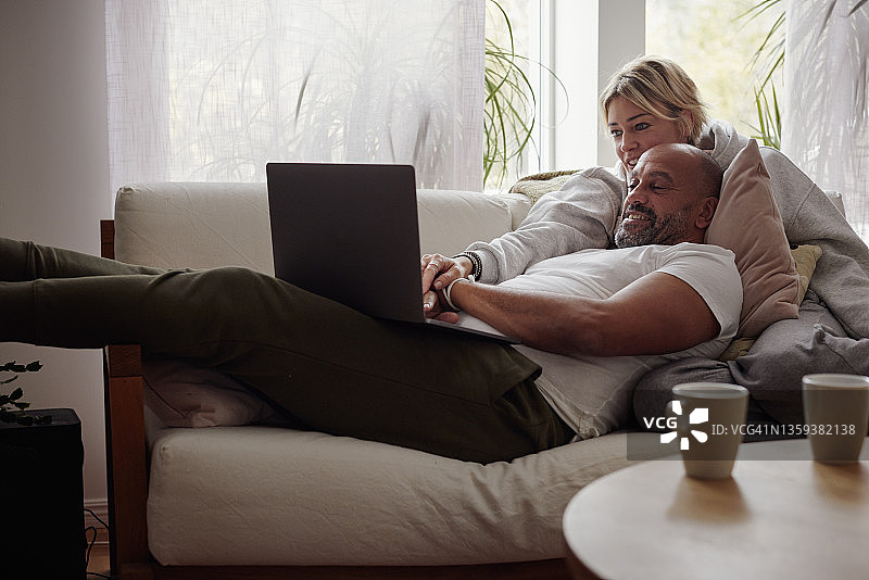 情侣躺在沙发上使用笔记本电脑图片素材