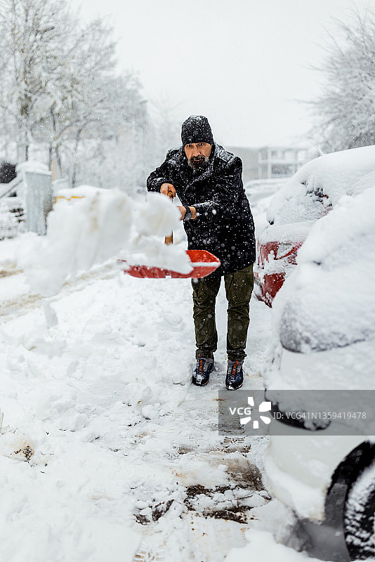 用雪铲铲雪的中年男人，雪下的汽车和街道图片素材