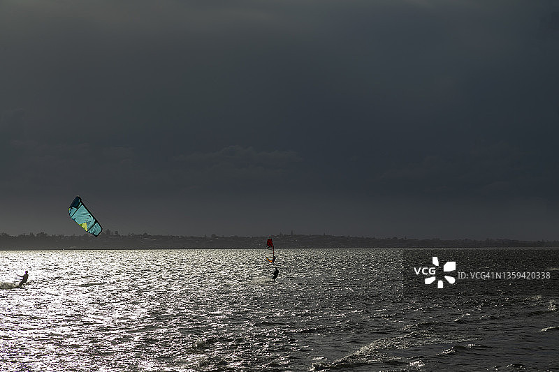 眺望暴风雨天空下的海面与日落时分的风筝冲浪者图片素材
