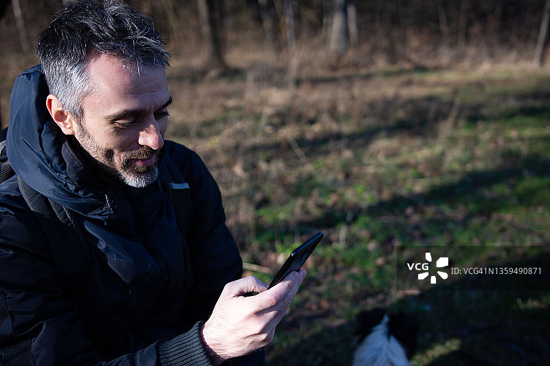 中年男子坐在公园的长椅上使用智能手机图片素材