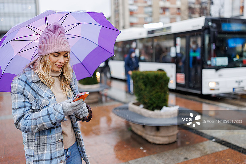 在城市里站立用手机打字的撑伞女人图片素材