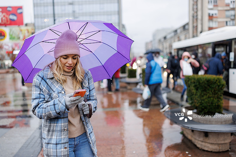 在城市里站立用手机打字的撑伞女人图片素材