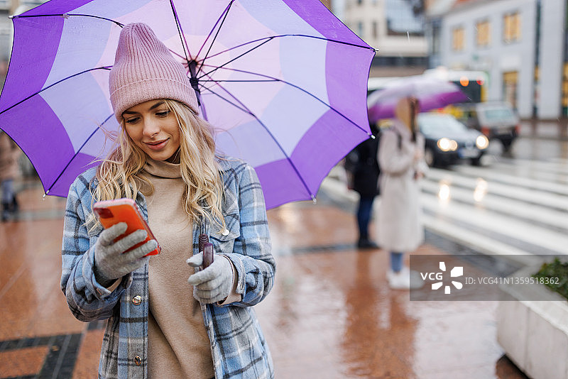 年轻女子在城市里雨天打伞发短信图片素材
