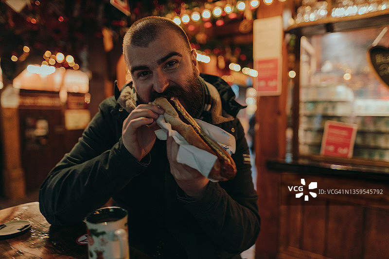 快乐的男人在圣诞市场吃香肠图片素材