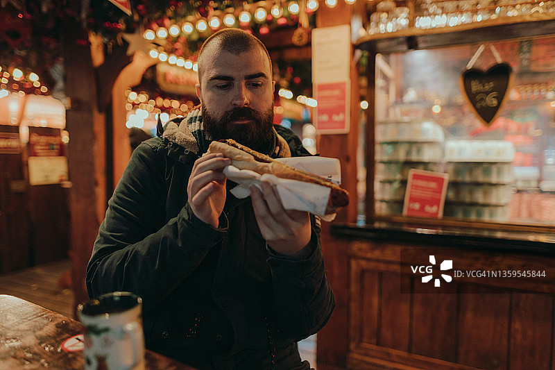 快乐的男人在圣诞市场吃香肠图片素材