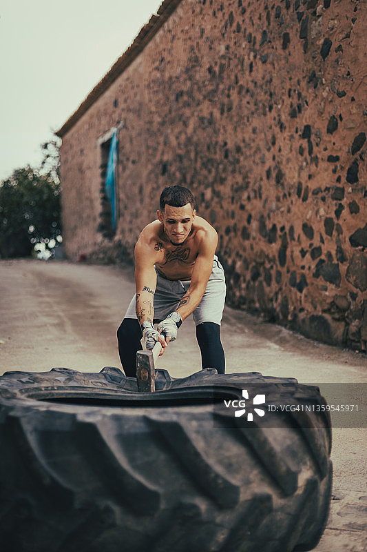 男孩在户外训练时用木槌敲击拖拉机轮图片素材