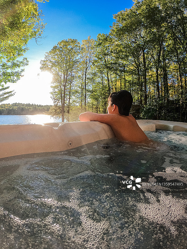 在享有湖景的小屋热水浴缸中放松的男孩图片素材