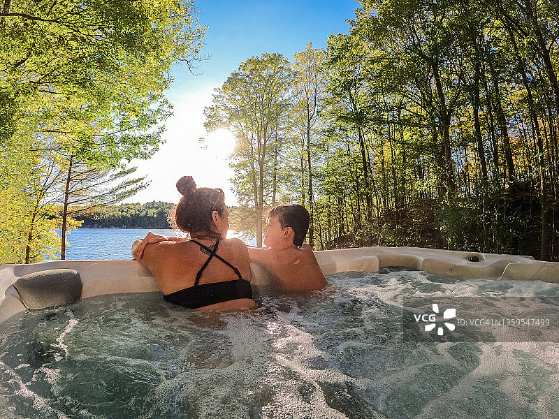 男孩和他的妈妈在可欣赏湖景的小屋热水浴缸里放松图片素材