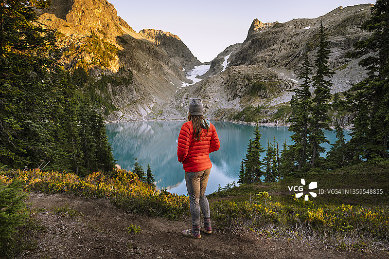 夕阳下身穿红色夹克的女人眺望蓝色高山湖泊图片素材