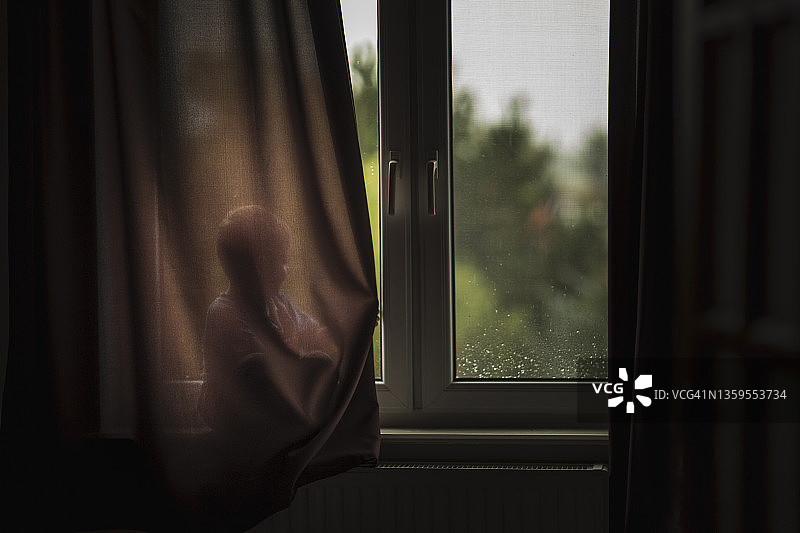 儿童坐在窗台上，躲在棕色窗帘后面图片素材