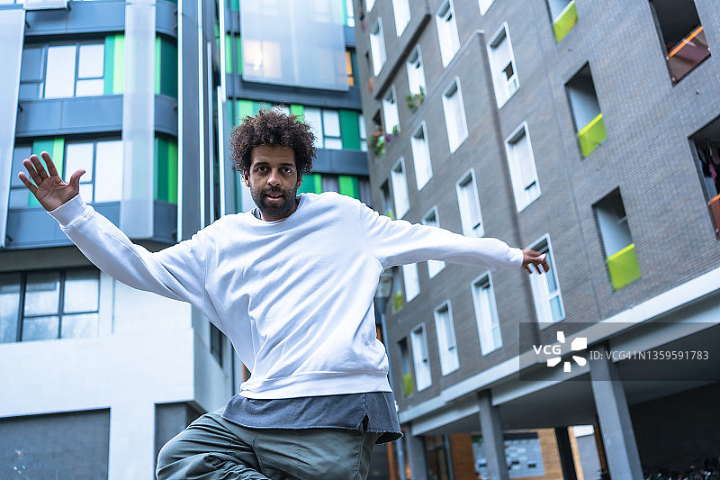 在彩色建筑中跳现代街舞的非裔发型白毛衣男子图片素材