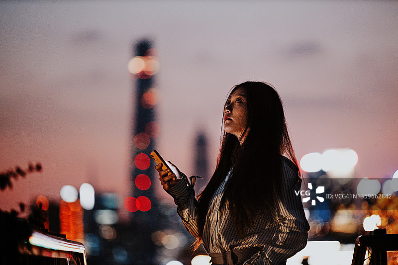 在上海金融区黄昏时分使用智能手机的年轻亚洲女性图片素材
