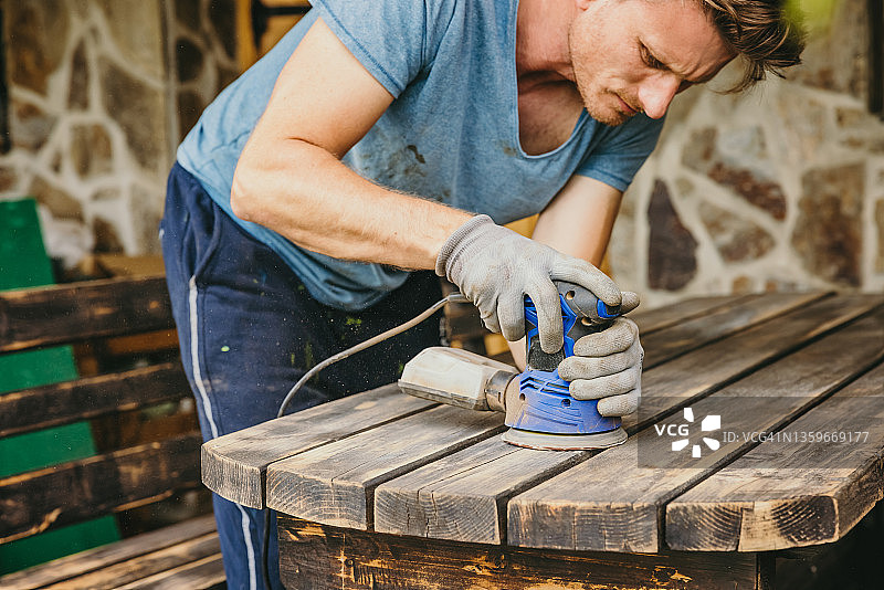 短发胡子男人在木桌上使用砂光机图片素材