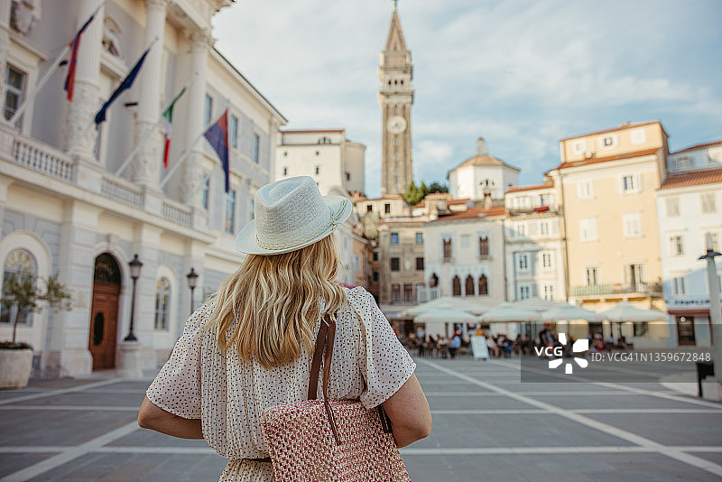 在斯洛文尼亚皮兰中心行走，背景是教堂塔楼的金发女人图片素材