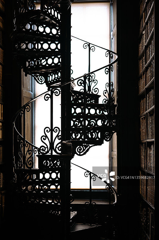 老旧图书馆：逆光下的书籍与旋转楼梯图片素材