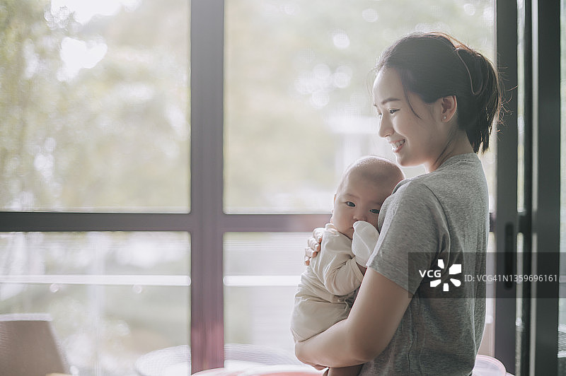 清晨，中国母亲抱着宝宝，沐浴在阳光中图片素材