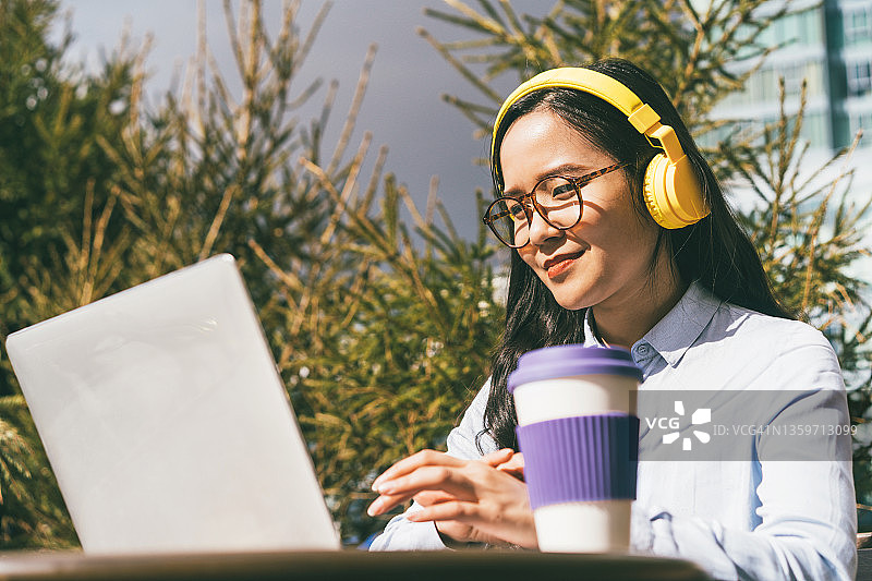 年轻漂亮的亚洲女子，身穿蓝色衬衫，戴着黄色耳机图片素材