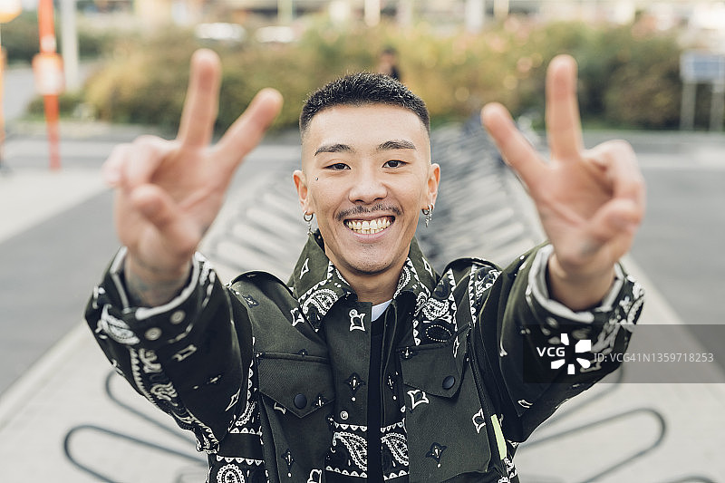 快乐的时尚男人在自行车站点附近做出和平标志图片素材