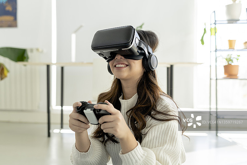 在家使用虚拟现实头显玩游戏控制器的微笑女人图片素材