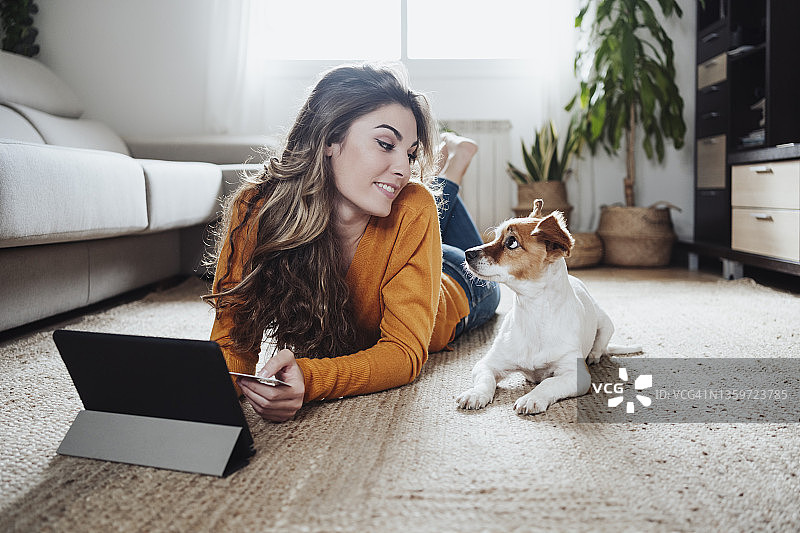年轻女子用平板电脑看着躺在地板上的宠物狗图片素材
