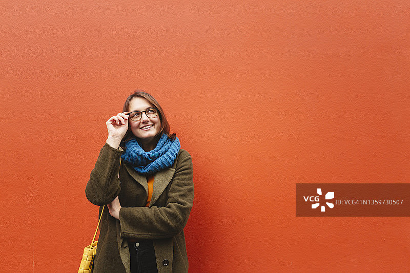 在橙色墙壁前戴眼镜的微笑女人图片素材