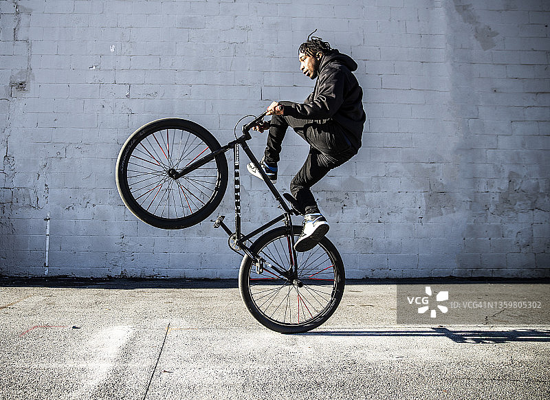 在城市地区表演前轮离地的年轻男性BMX骑手图片素材