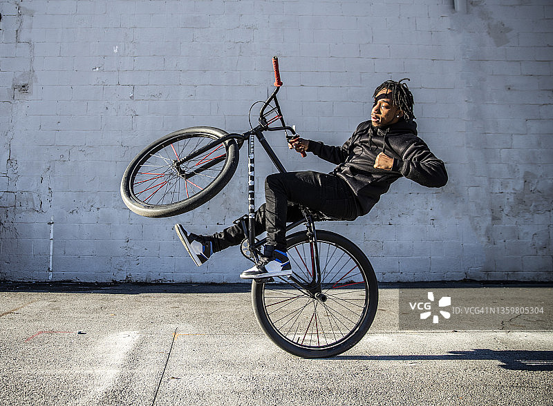 在城市地区表演前轮离地的年轻男性BMX骑手图片素材