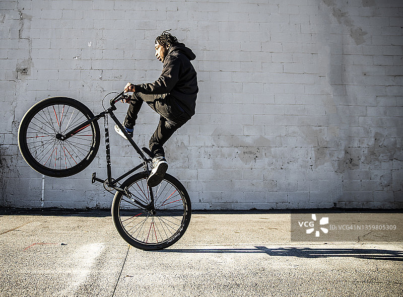 在城市地区表演前轮离地的年轻男性BMX骑手图片素材