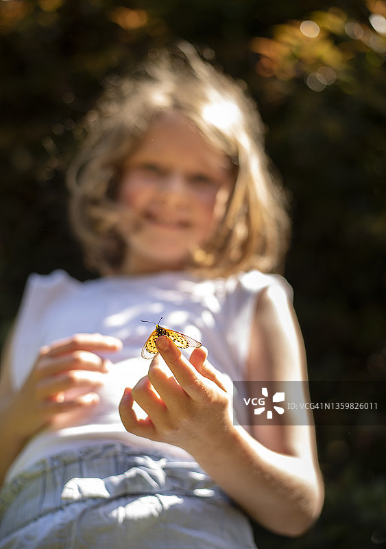 夏天，微笑的小女孩在户外拿着蝴蝶图片素材
