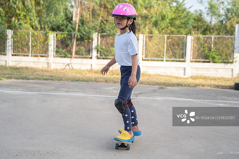 在美丽的夏日，可爱的小女孩在户外学习滑板图片素材