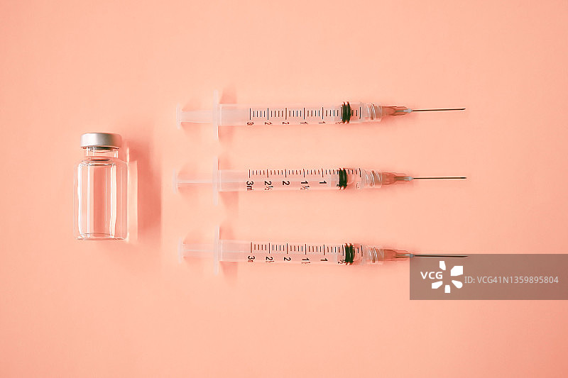 橙色背景上的三个带针头的注射器和医疗药瓶图片素材