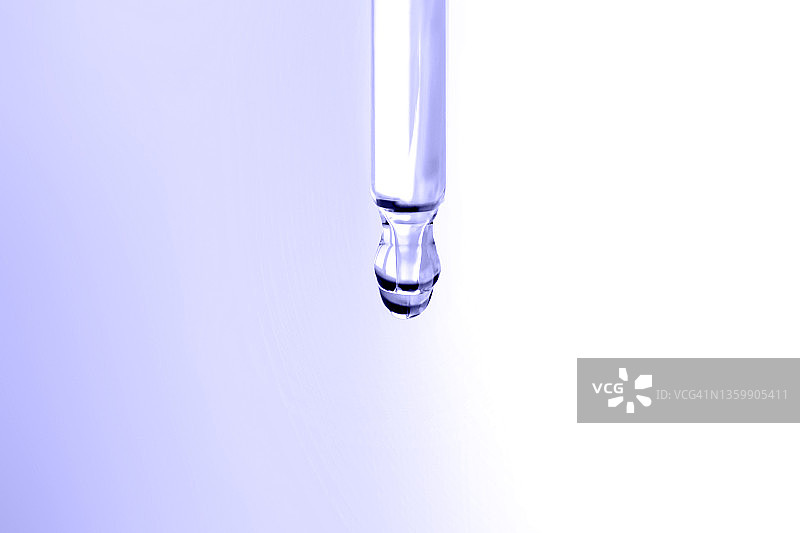 从玻璃滴管落在渐变紫白色背景上的紫色保湿乳液滴。微距摄影。展示2022年的代表色图片素材