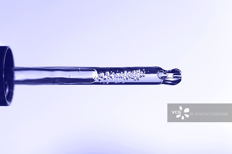 白色背景上带有紫色液体保湿乳液的玻璃滴管。微距摄影。展示2022年的长春花蓝图片素材