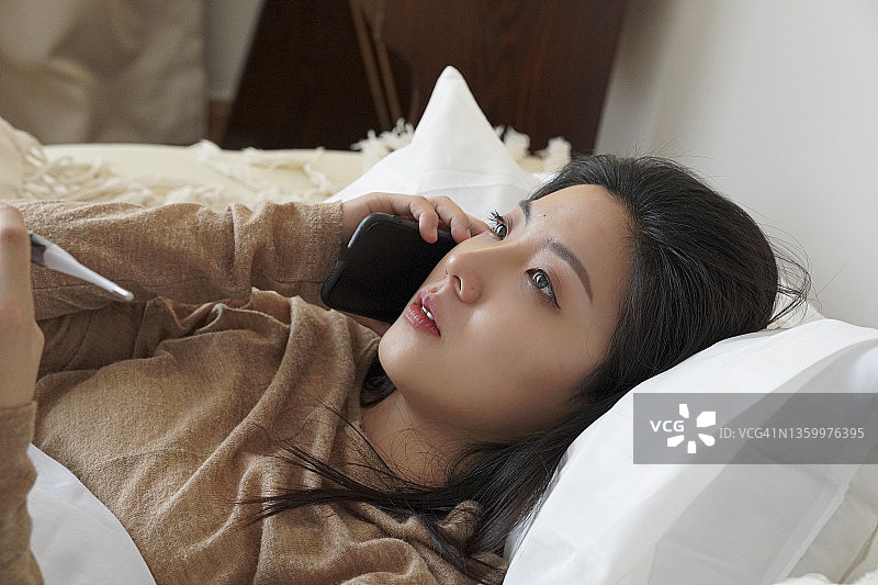 生病的亚洲女人在床上打电话给医生图片素材