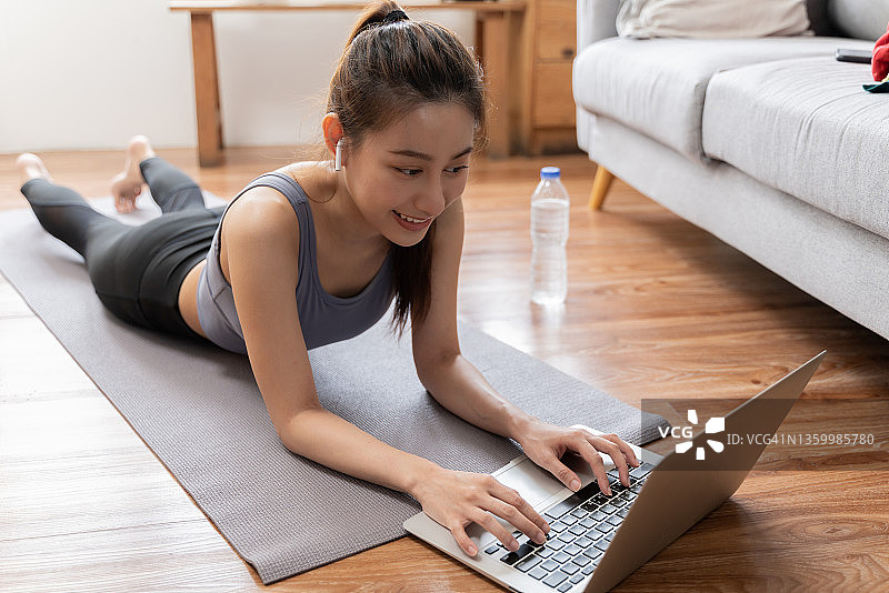 迷人的年轻女人在家用笔记本电脑锻炼图片素材