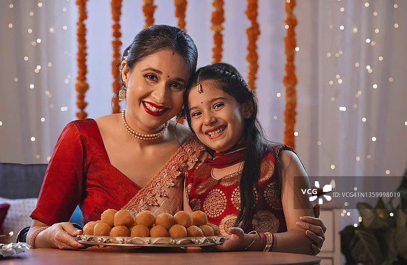 母亲和女儿坐在盘子里，盘子里装着ladous，后面是排灯节装饰和灯光图片素材