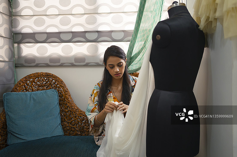 年轻女子坐着，用别针整理人体模型上的服装图片素材