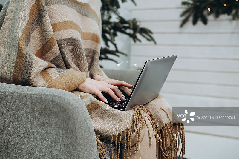 靠在木墙和圣诞树旁用笔记本电脑工作的年轻女人图片素材