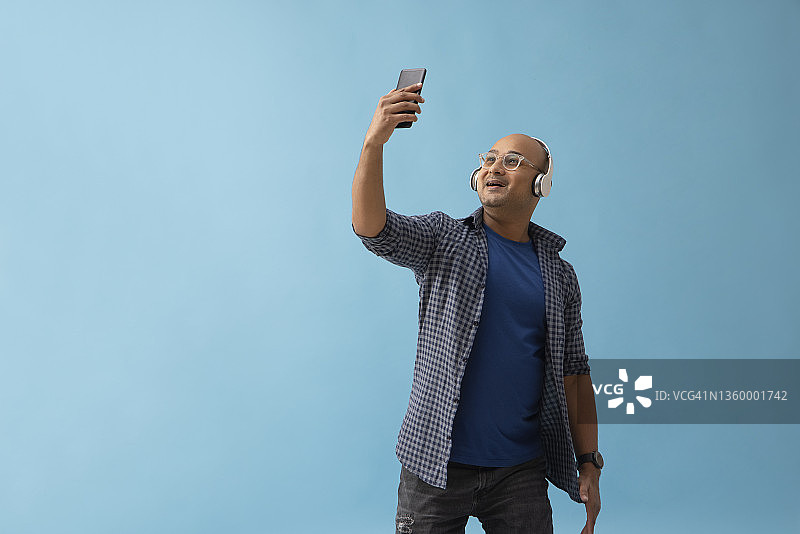 简朴背景下，戴着耳机进行视频通话的秃头男人肖像图片素材