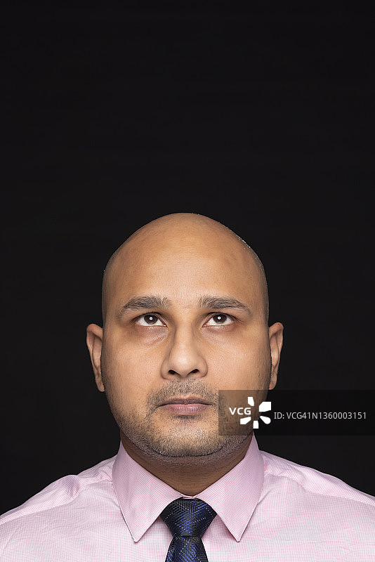 黑色背景下，穿着正装向上翻白眼的秃头男人肖像图片素材