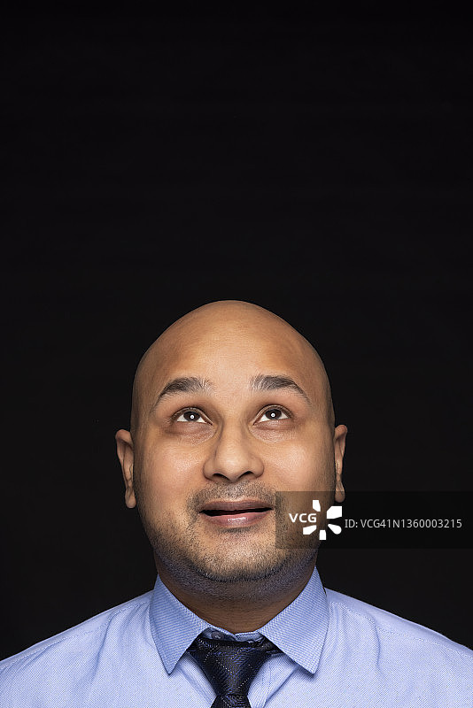 黑色背景下，穿着正装向上翻白眼的秃头男人肖像图片素材