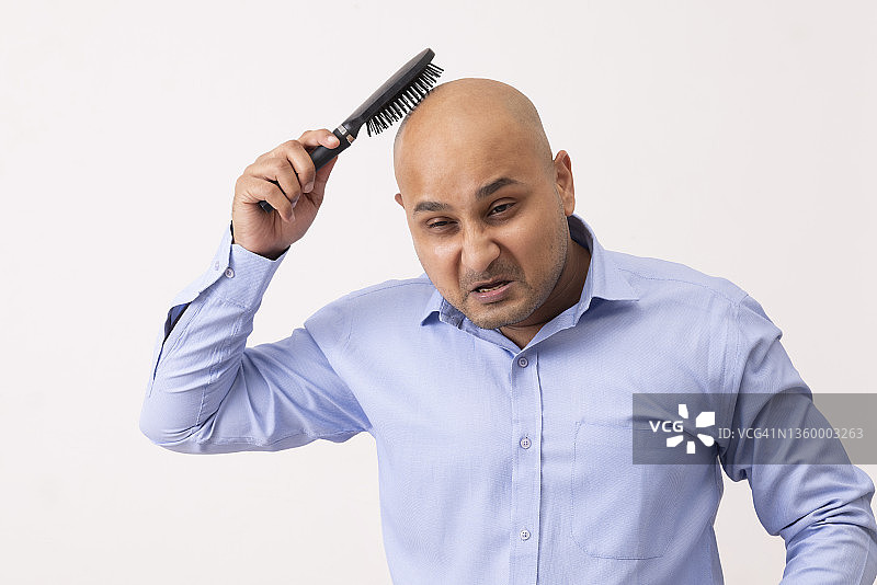 一个秃顶男人沮丧地梳理着剃光的头，白色背景图片素材