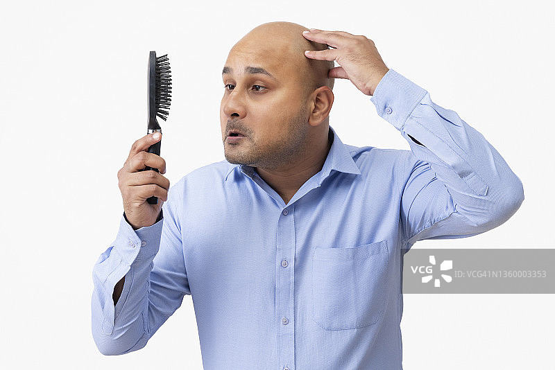 看着手中的梳子，摸着光头，面露悲伤的男人肖像图片素材