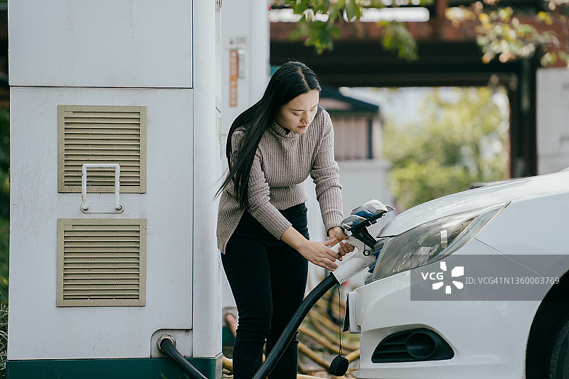 亚洲女人正在为她的电动汽车充电图片素材